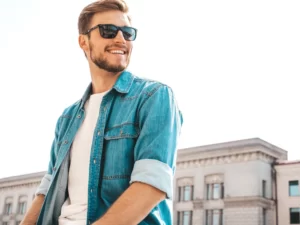 A man wearing sunglasses and a denim shirt over a white t-shirt